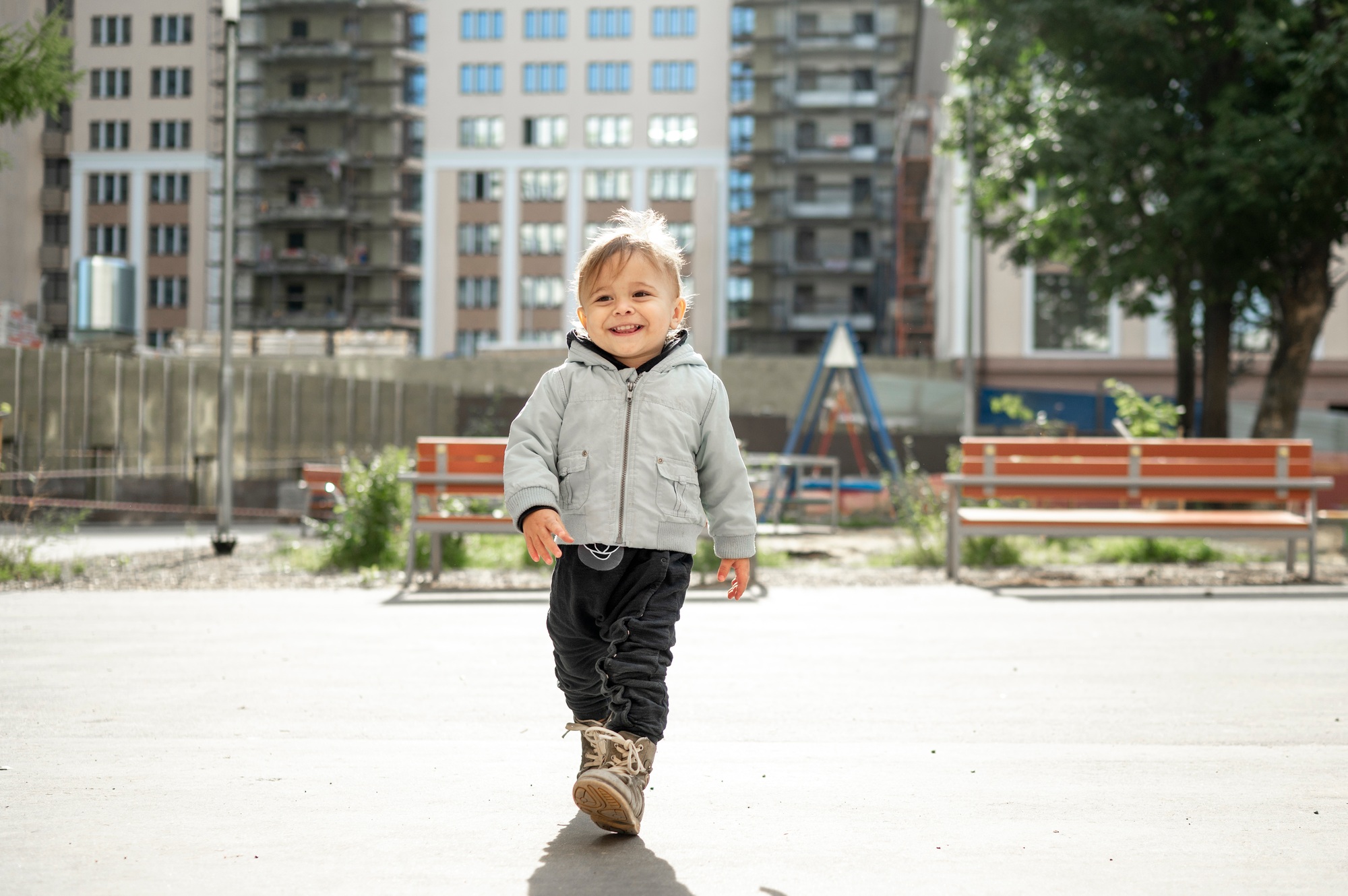 A kid walks on a children's playground in the courtyard of an apartment building
